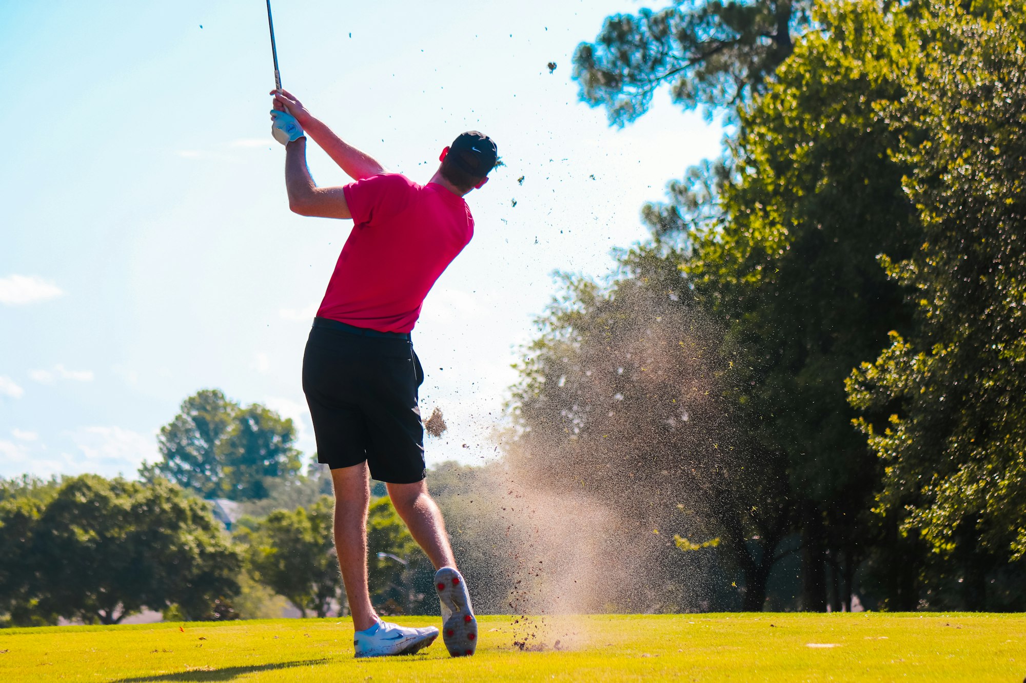 A man in a red shirt and black shorts swings at a golf ball