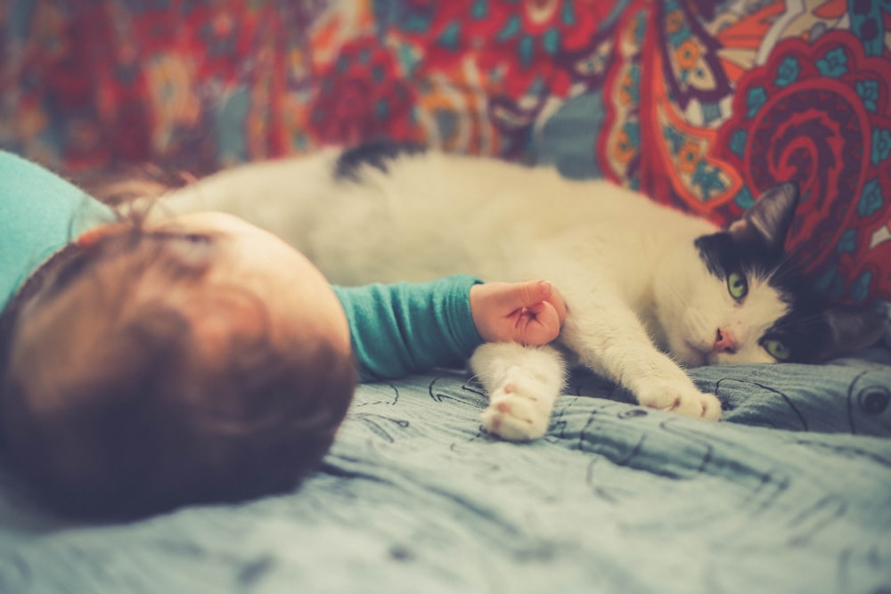 white and black cat lying beside baby