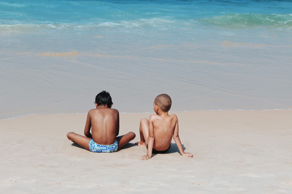 two topless children sitting near seashore during daytime