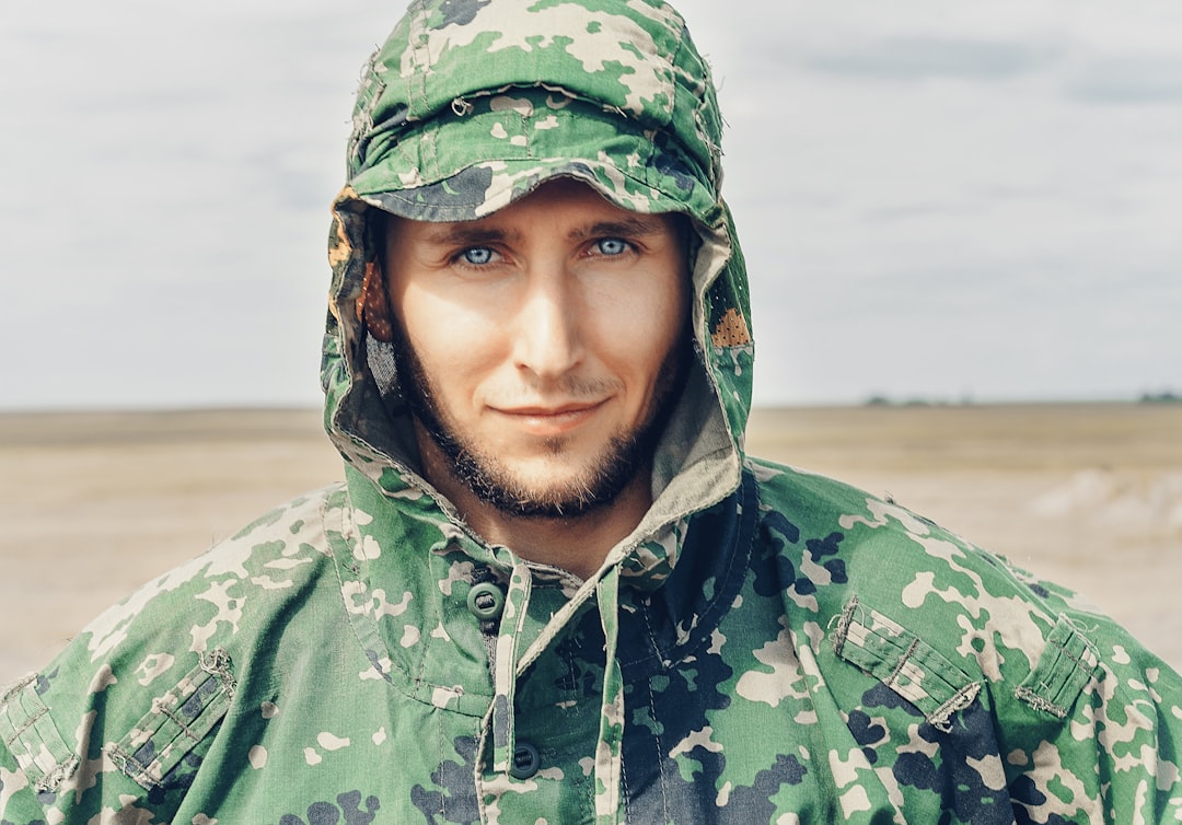 man wearing camouflage hooded top looking at the camera during day