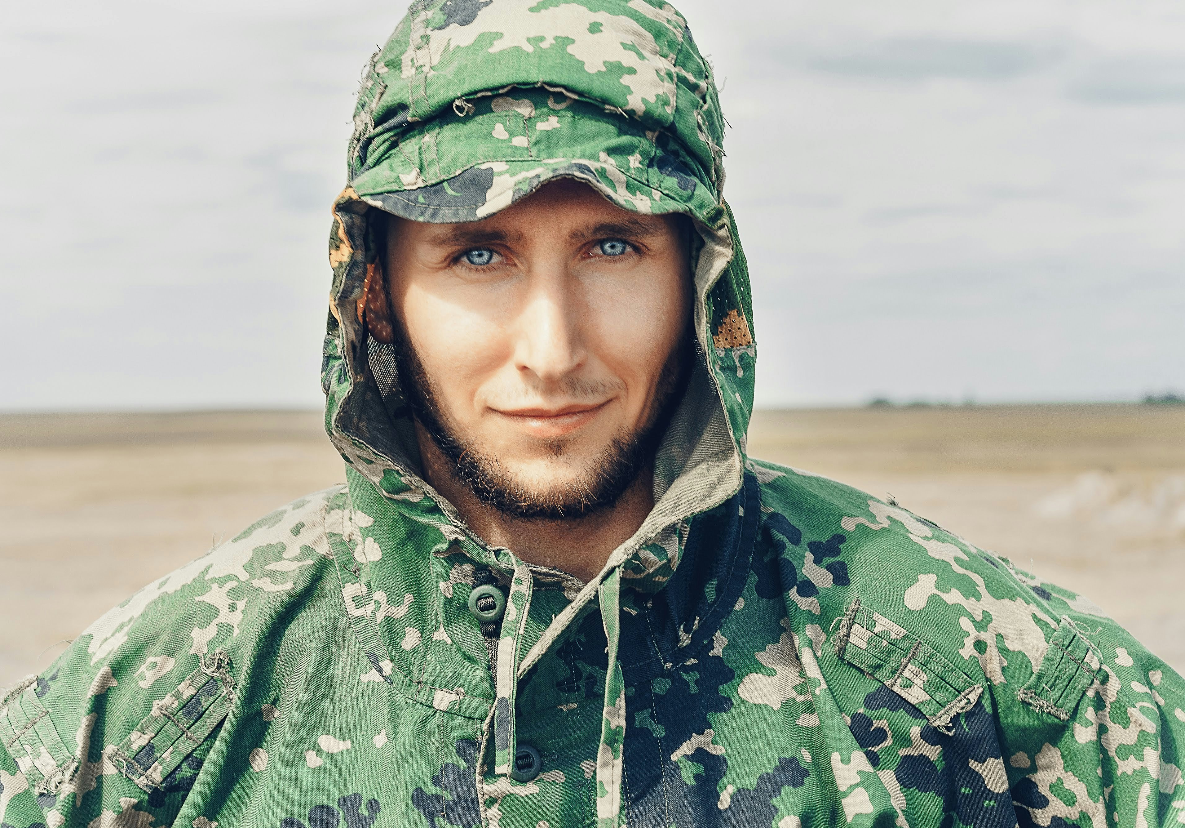 man wearing camouflage hooded top looking at the camera during day