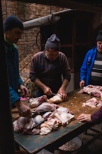 A group of local farmers gathered around a table outdoors, discussing plans with feed bags and farm tools in the background.