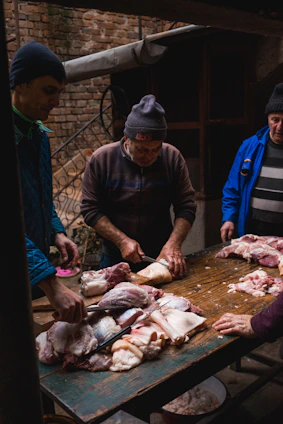 A group of local farmers gathered around a table outdoors, discussing plans with feed bags and farm tools in the background.
