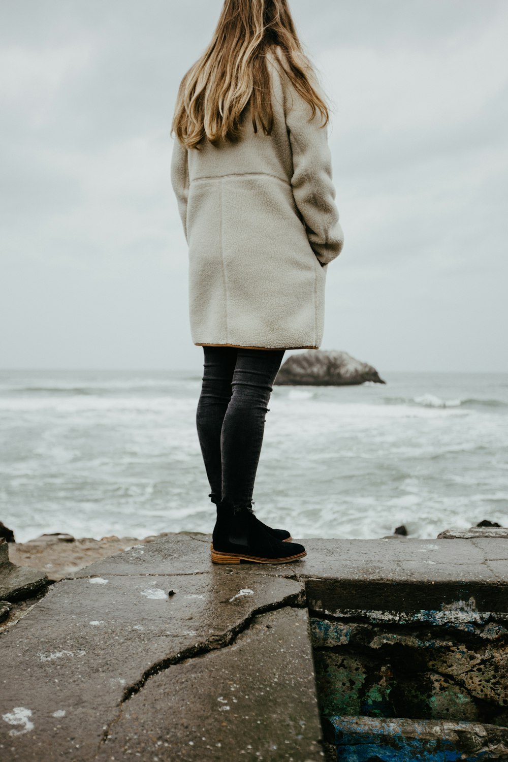 바닷가에 서 있는 갈색 코트를 입은 여자