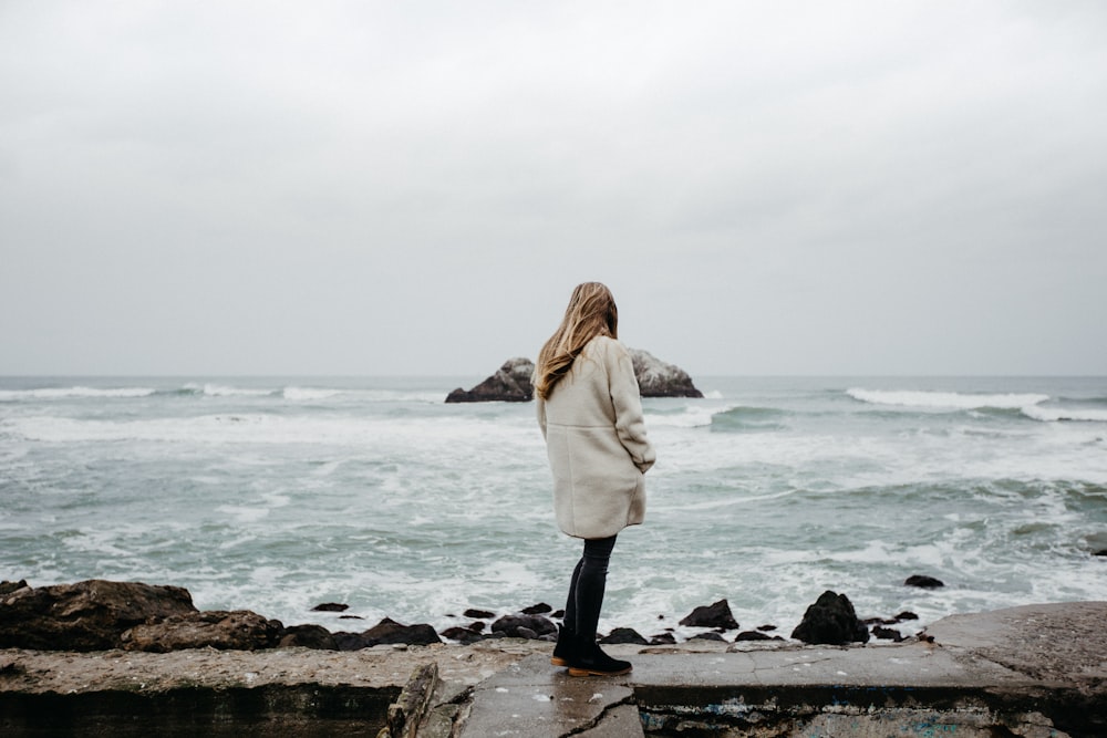 a woman standing on the edge of a cliff overlooking the ocean