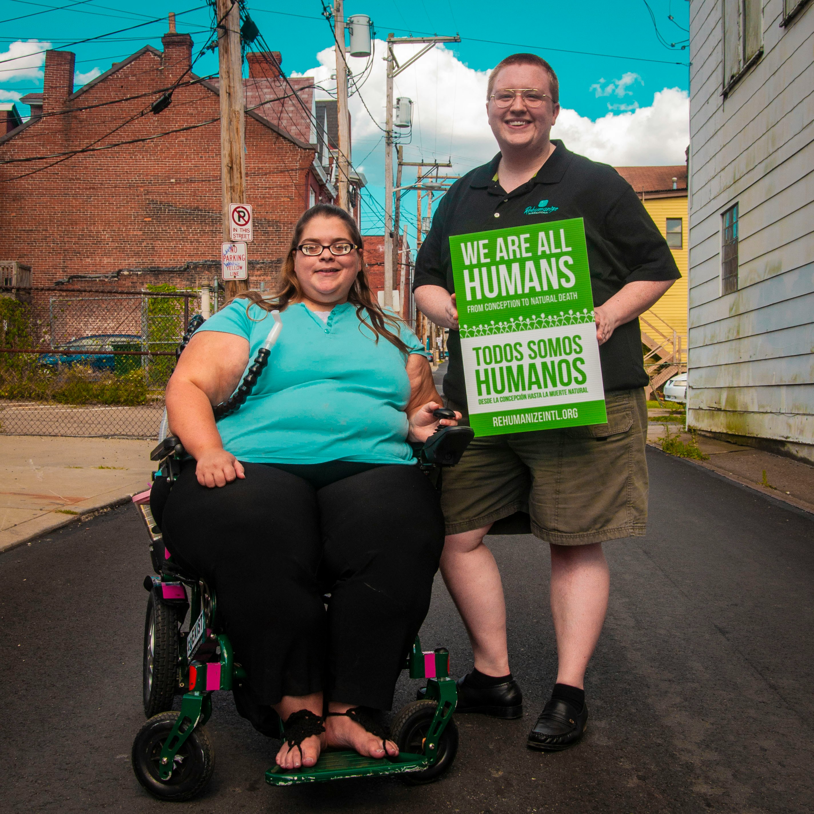 woman sitting on wheelchair beside man holding we are all humans sign