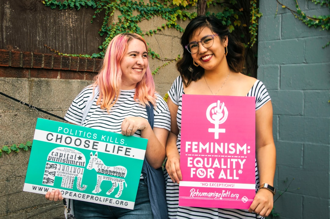 two smiling women standing while holding banners near concrete wall