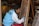 A person is focused on painting a colorful intricate design on a canvas, wearing a blue and white jacket with 'MCFC' on the back. The scene is set in what appears to be an artist's workshop, with various art supplies and other framed artworks visible.