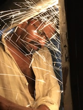 Artist Marte Cellura welding a large metal sculpture in the studio, sparks flying around.