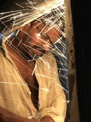 Close-up of a faded navy tie-dye shirt framed with welding tools and sparks flying softly in the background.