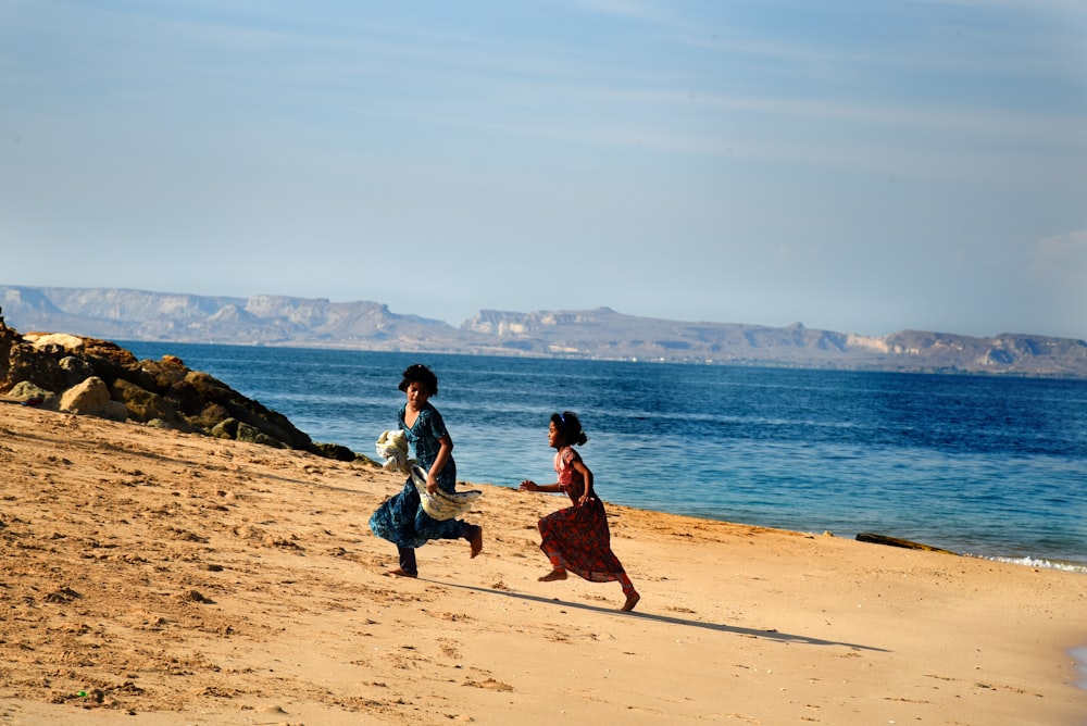 two girls running on sand seashore during day