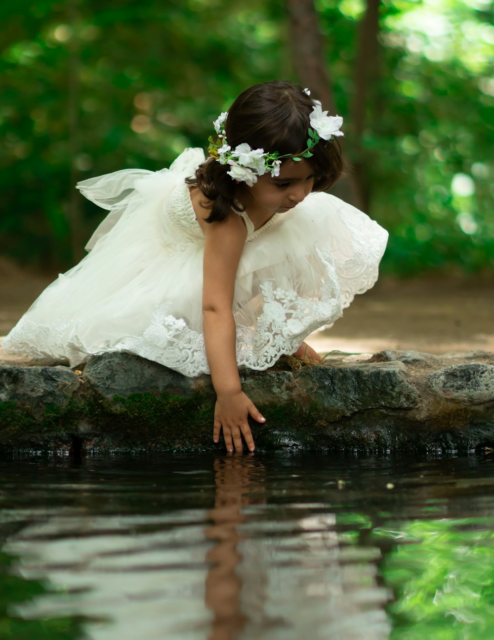 girl in white dress reaching for water in puddle