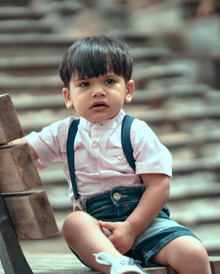 A toddler in a cozy pastel pink hoodie and matching joggers sitting on a minimalist white bench.