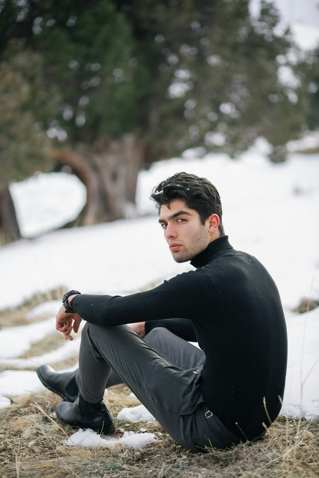 man in black long sleeve shirt and gray pants sitting on gray concrete floor during daytime