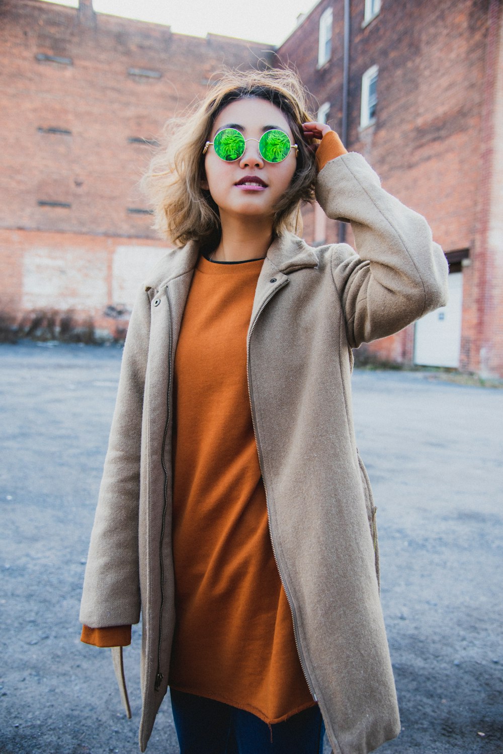 femme portant une veste zippée grise et des lunettes de soleil debout tout en touchant ses cheveux