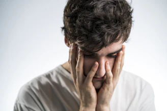 A person sitting with their head in their hands, looking clearly overwhelmed in a soft, neutral-toned room.