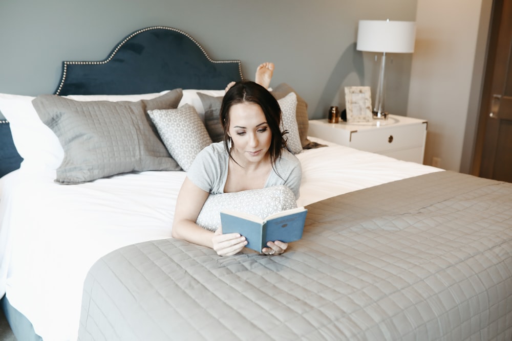 woman lying forward on bed while reading book