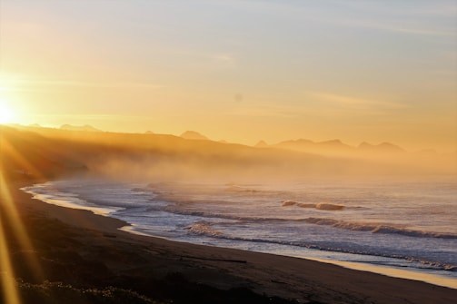 A peaceful shoreline at dawn with soft cream and brown tones blending into the water.