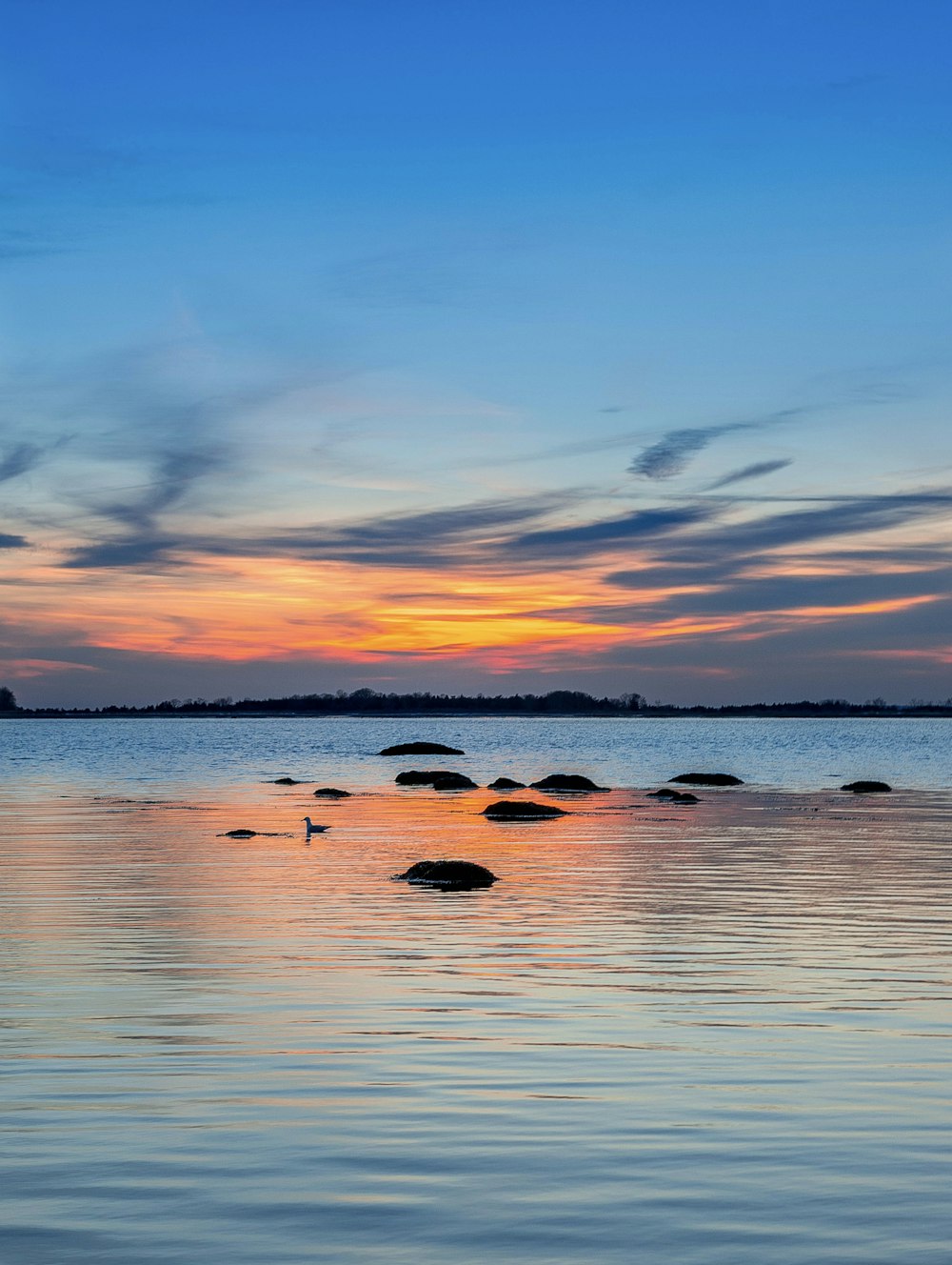 gray rock formations on body of water under blue and orange sky