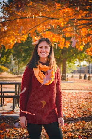 A smiling woman wearing a warm wool scarf while walking through autumn leaves.
