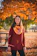 A smiling woman wearing a custom hoodie, standing outdoors on a crisp autumn day.
