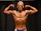 Athlete posing confidently on stage during fitness competition with supportive coach nearby