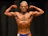 Athlete posing confidently on stage during fitness competition with supportive coach nearby