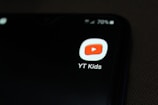 A smartphone screen displaying the YT Kids app icon, which features a red play button inside a white rounded square. The icon is prominently displayed against a dark background, with a battery icon at the top right corner showing 70% charge.