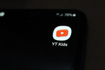 A smartphone screen displaying the YT Kids app icon, which features a red play button inside a white rounded square. The icon is prominently displayed against a dark background, with a battery icon at the top right corner showing 70% charge.