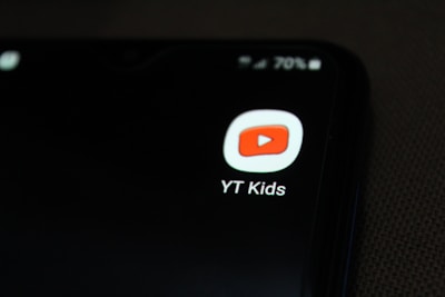 A smartphone screen displaying the YT Kids app icon, which features a red play button inside a white rounded square. The icon is prominently displayed against a dark background, with a battery icon at the top right corner showing 70% charge.