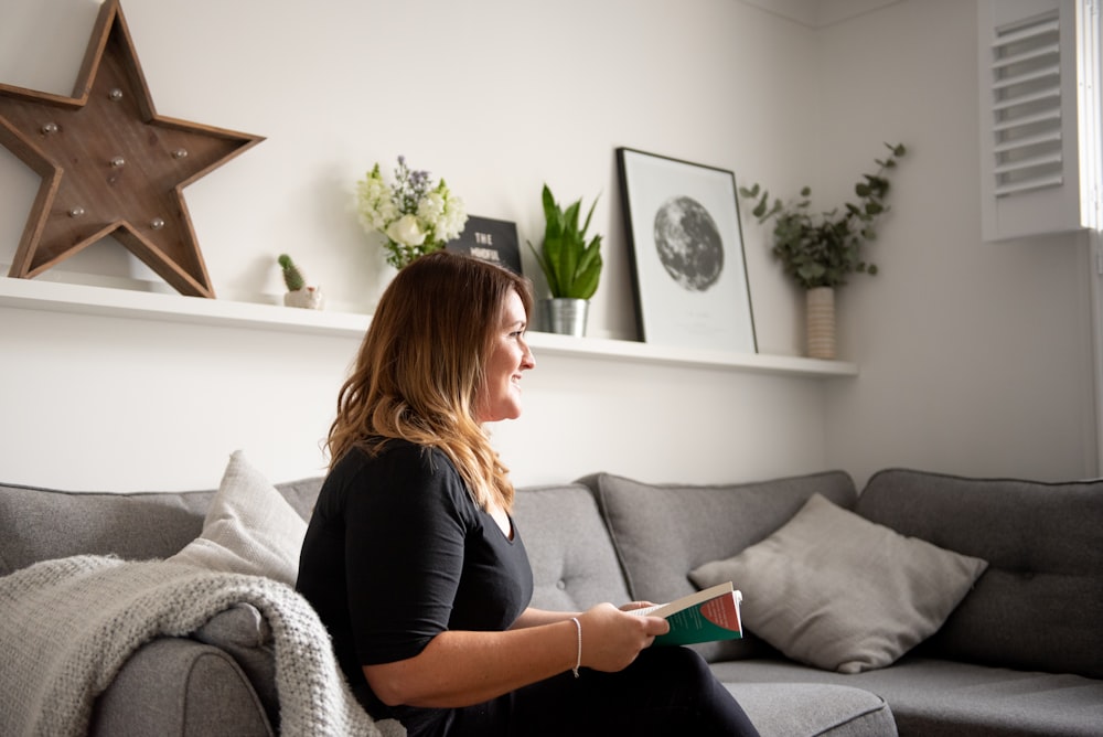 Lächelnde Frau sitzt auf dem Sofa und hält ein Buch in der Hand