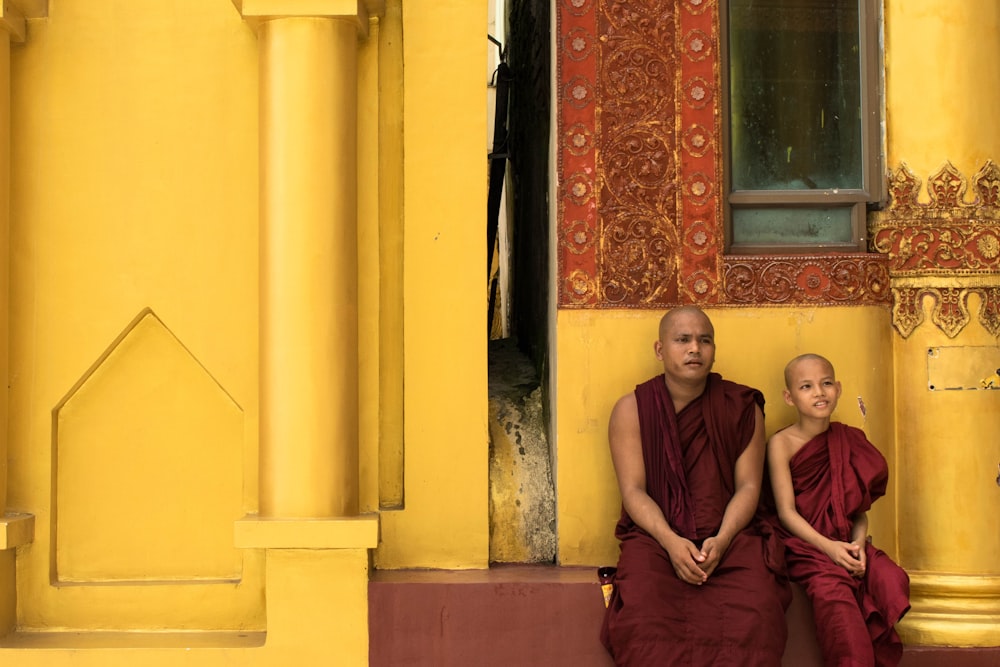 two monks sit outside yellow painted building
