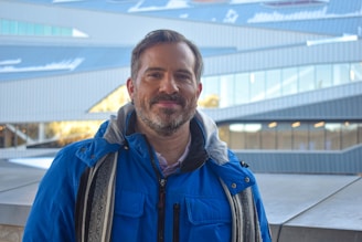 A smiling man wearing a deep blue scarf wrapped casually around his neck on a crisp autumn day.