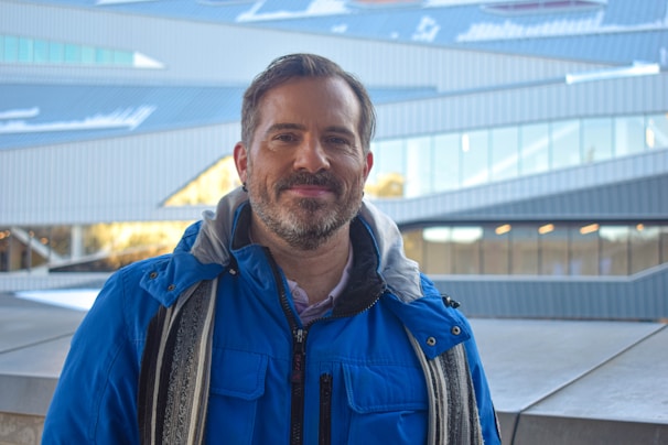 A man wearing a deep blue cottonhue scarf, smiling on a crisp autumn day in the park.