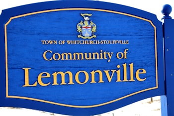 A sign with a blue background and yellow text, displaying 'Town of Whitchurch-Stouffville' and 'Community of Lemonville'. It also features a coat of arms above the text.