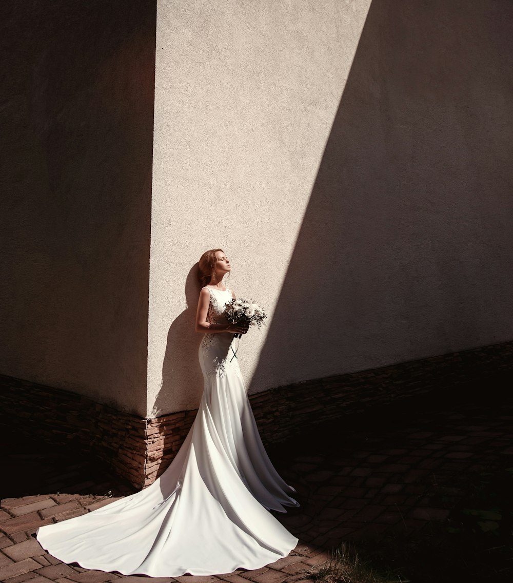 woman standing beside wall holding flowers