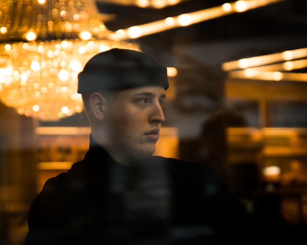 uomo seduto accanto al pannello di vetro che indossa un berretto lavorato a maglia nero