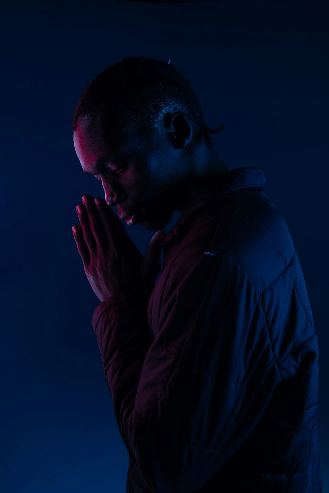 man wearing black bubble jacket with praying hands standing while facing his right side