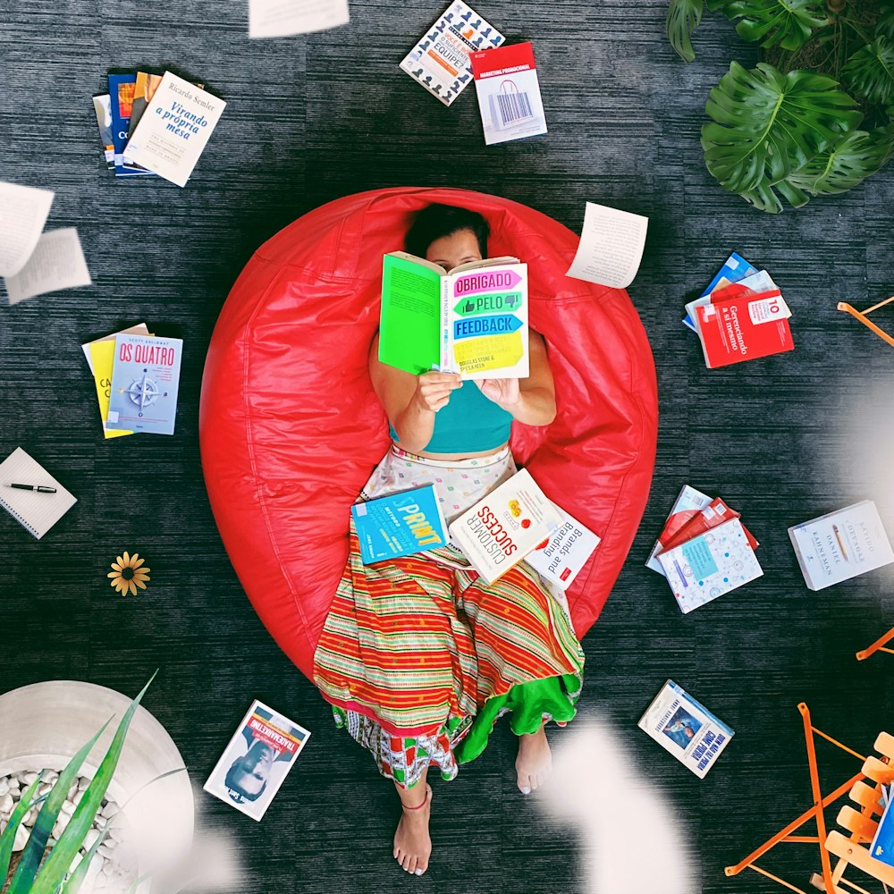 mulher deitada no pufe vermelho lendo livro