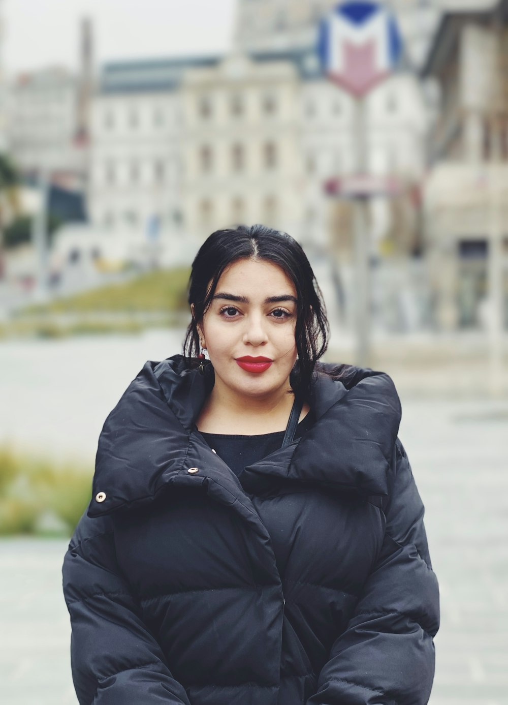 woman taking a photo wearing black bubble jacket standing in front of white building