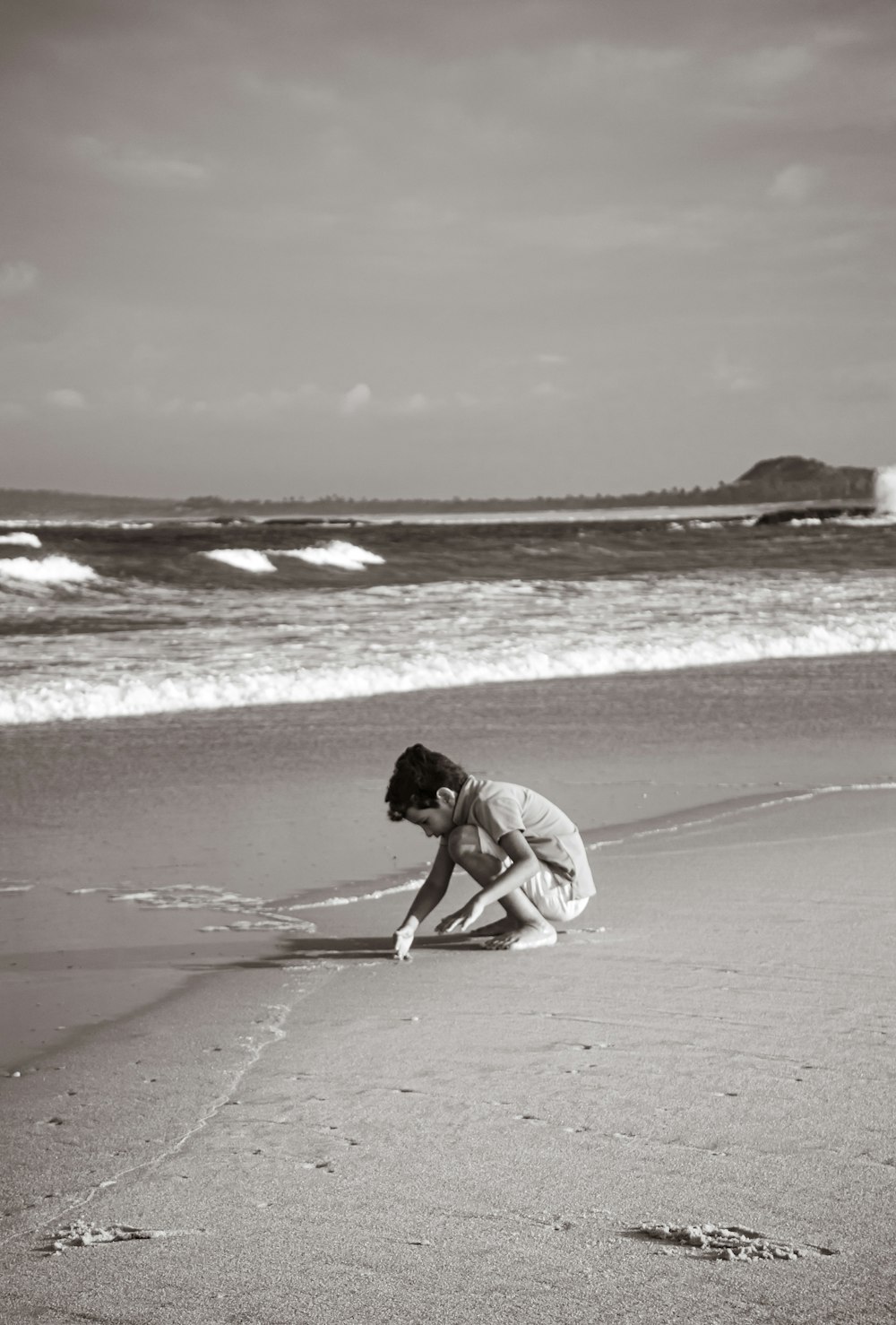 grayscale photo of boy sitting in front of shoreline