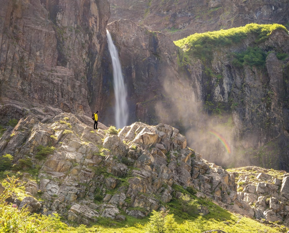 person on mountain cliff near waterfalls