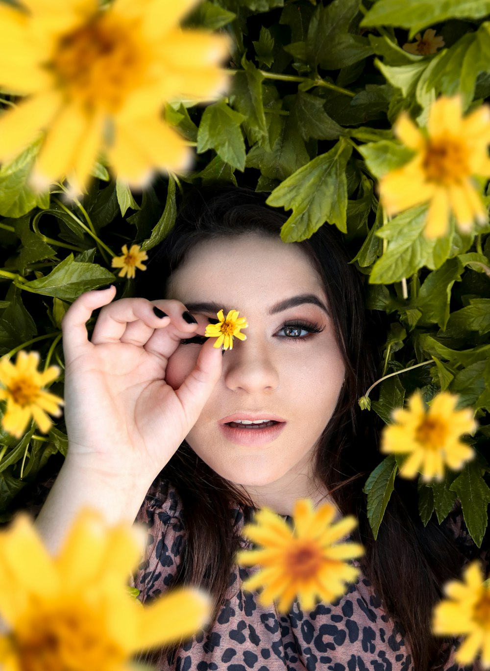 woman in black shirt smiling and standing beside yellow flowers