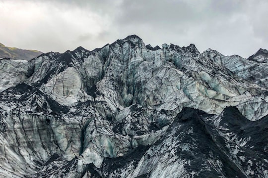 gray rocky mountain under cloudy sky during daytime in Sólheimajökull Iceland