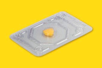 A single yellow pill is encased in a transparent blister pack made of plastic or foil. The background is a solid bright yellow, emphasizing the pill and its packaging.