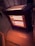 A portable electric heater with visible glowing heating elements is positioned on a polished floor. The heater is plugged in with a black cord extending from it. Ornate furniture and decorative molding can be seen in the background, adding to the cozy indoor atmosphere.