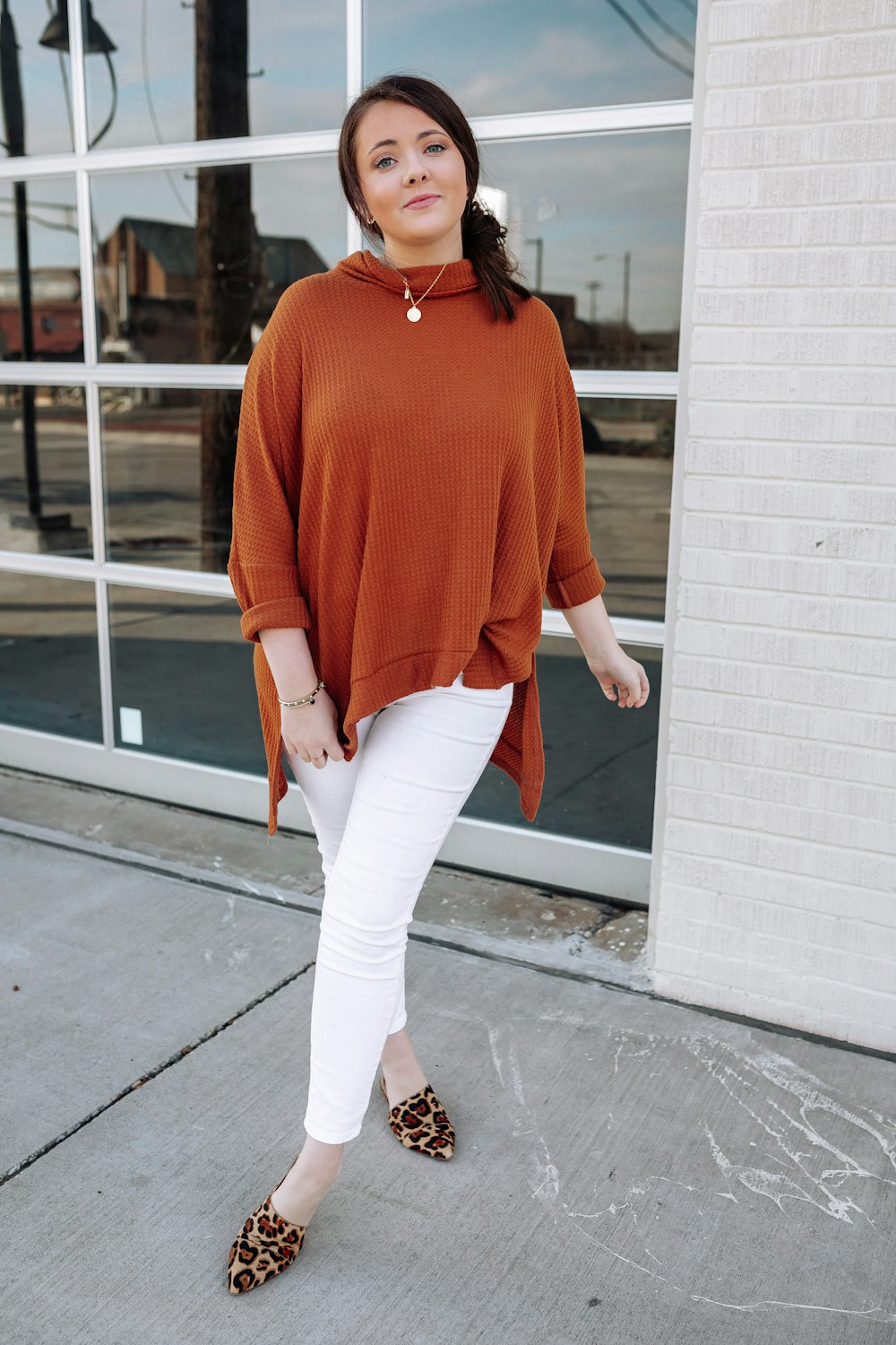 a woman wearing a brown sweater and white pants