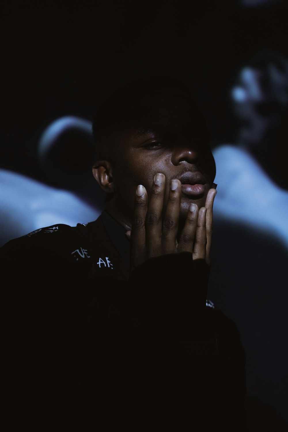 man in black crew neck shirt covering his face with his hand