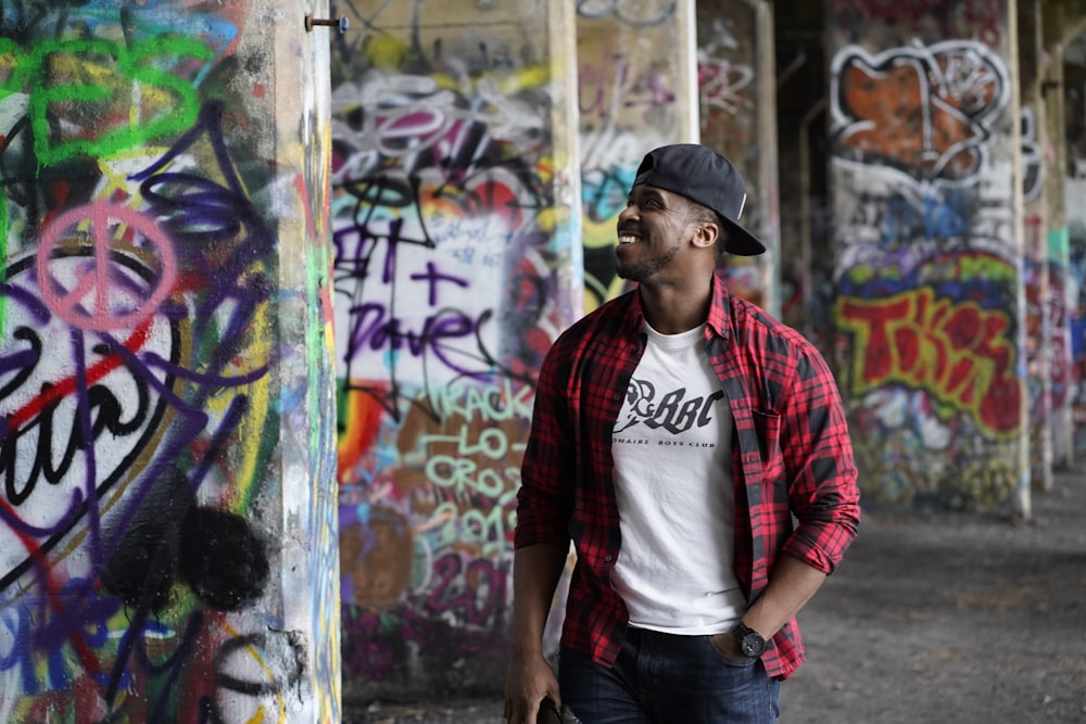 man in red and black plaid dress shirt and blue denim jeans standing beside graffiti wall