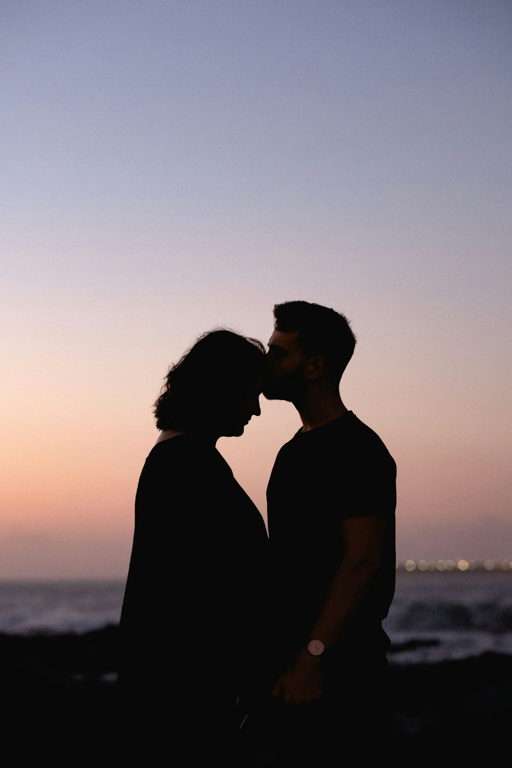 silhouette of man and woman standing near body of water during sunset